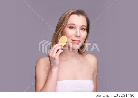 Young caucasian female using exfoliating sponge for skincare on gray background Young caucasian female using exfoliating sponge for skincare on gray background 133251480