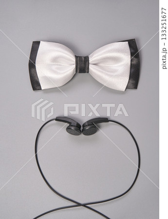 Elegant white bow tie and black earbuds on gray background for fashion and music Elegant white bow tie and black earbuds on gray background for fashion and music 133251677