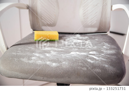 Yellow sponge on gray dirty upholstery of computer chair with foam. Concept of cleaning upholstered furniture at home, close-up. Industry 133251731
