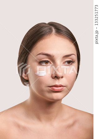 Young caucasian female with facial cream on cheek for skincare routine Young caucasian female with facial cream on cheek for skincare routine 133251773