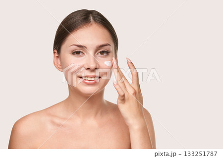 Young caucasian female applying face cream smiling in skincare routine portrait Young caucasian female applying face cream smiling in skincare routine portrait 133251787