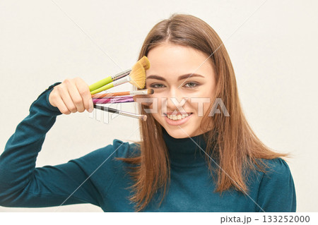 Young caucasian female smiling with makeup brushes against face in casual 133252000