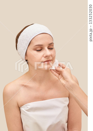 Caucasian female adult skincare routine with cotton pad and headband on neutral Caucasian female adult skincare routine with cotton pad and headband on neutral 133252030