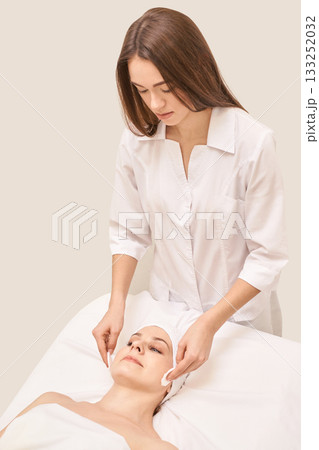 Young caucasian female therapist applying skincare treatment to relaxed adult Young caucasian female therapist applying skincare treatment to relaxed adult 133252032
