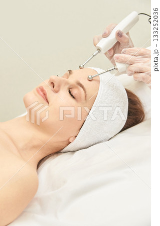 Young caucasian female receiving facial microcurrent therapy in spa setting 133252036