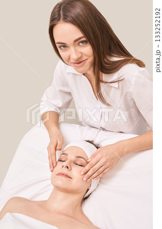 Caucasian female beautician giving relaxing facial massage to adult woman 133252192