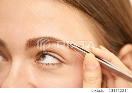Young caucasian female using tweezers for eyebrow grooming close-up Young caucasian female using tweezers for eyebrow grooming close-up 133252214