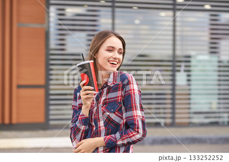 Young caucasian female holding drink cup and smiling outdoors in casual plaid 133252252