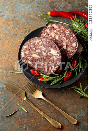 Spanish black pudding or blood sausage accompanied by rosemary and red pepper on a black plate. Spanish black pudding or blood sausage accompanied by rosemary and red pepper on a black plate. 133252393