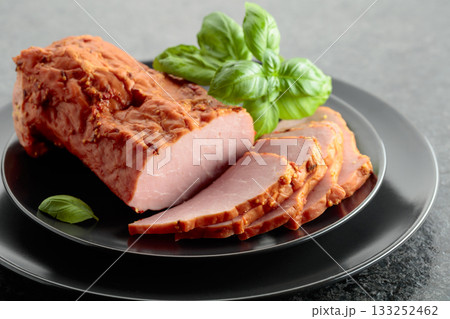 Smoked ham with basil on a black plate. 133252462