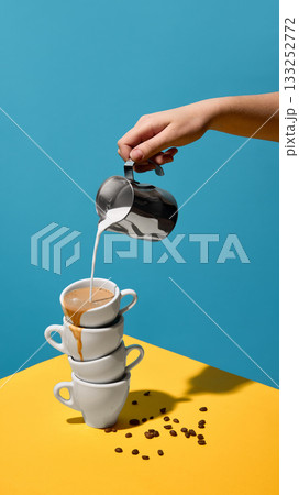 Hand pouring milk into stacked coffee cups on color background 133252772
