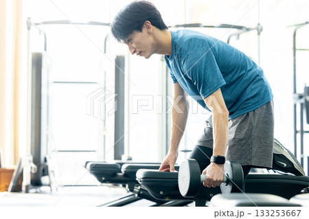 トレーニングジムでダンベルを使って筋トレする若い男性 133253667