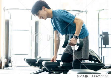 トレーニングジムでダンベルを使って筋トレする若い男性 133253668