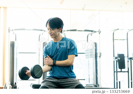 トレーニングジムでダンベルを使って筋トレする若い男性 133253669