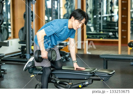 トレーニングジムでダンベルを使って筋トレする若い男性 133253675