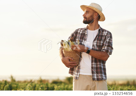 Paper package with corn in hands. Farmer is on the agricultural field Paper package with corn in hands. Farmer is on the agricultural field 133254656