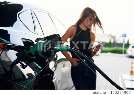 Smartphone in hands. A young woman at a gas station with her car 133254906