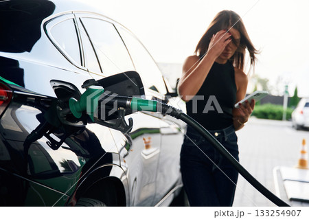 Smartphone in hands. A young woman at a gas station with her car 133254907