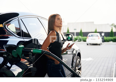 Smartphone in hands. A young woman at a gas station with her car Smartphone in hands. A young woman at a gas station with her car 133254909
