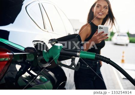 Waiting, holding smartphone. A young woman at a gas station with her car 133254914