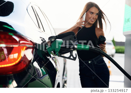 Talking by a phone. A young woman at a gas station with her car 133254917