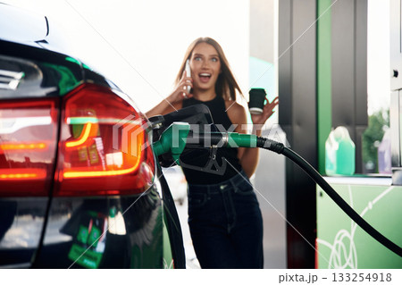 Talking by a phone. A young woman at a gas station with her car 133254918