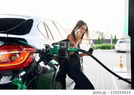Talking by a phone. A young woman at a gas station with her car 133254919