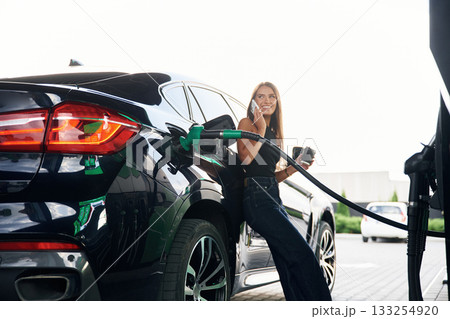 Having a conversation by phone. A young woman at a gas station with her car 133254920
