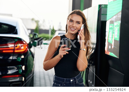 Having a conversation by phone. A young woman at a gas station with her car Having a conversation by phone. A young woman at a gas station with her car 133254924