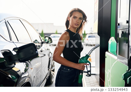 Pump nozzle in the hand. A young woman at a gas station with her car Pump nozzle in the hand. A young woman at a gas station with her car 133254943