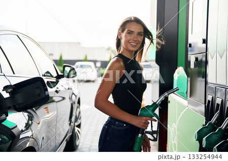 Smiling, standing and posing. A young woman at a gas station with her car Smiling, standing and posing. A young woman at a gas station with her car 133254944
