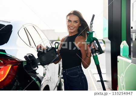 Smiling, standing and posing. A young woman at a gas station with her car 133254947
