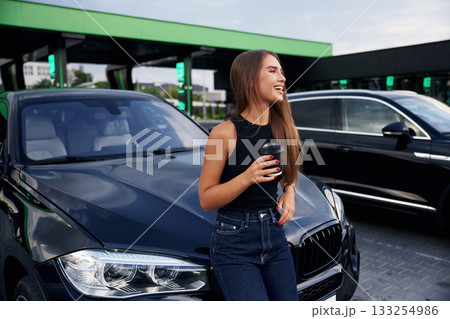 Front view, standing. A young woman at a gas station with her car 133254986