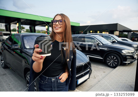 Happy owner with cup of drink. A young woman at a gas station with her car 133255099