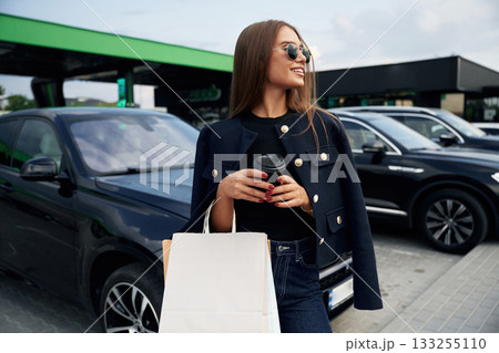 Shopping bags in hand. A young woman at a gas station with her car 133255110