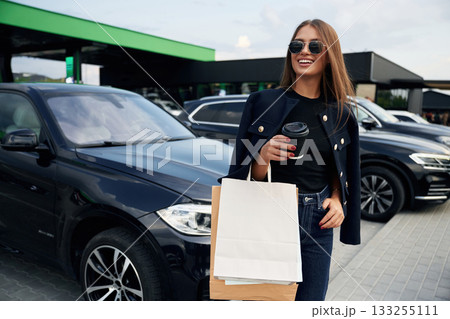 Shopping bags in hand. A young woman at a gas station with her car 133255111