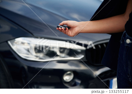 Focused close up view of woman hand that is holding key in front of the car 133255117