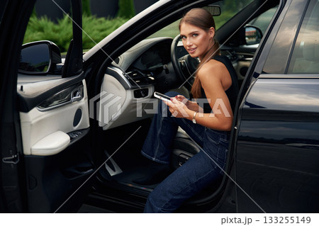 Looking at camera, holding smartphone. Woman is sitting in the car Looking at camera, holding smartphone. Woman is sitting in the car 133255149