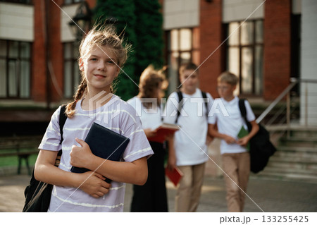 Portrait of girl that is standing in front of her friends. Kids are near the school together, pupils 133255425