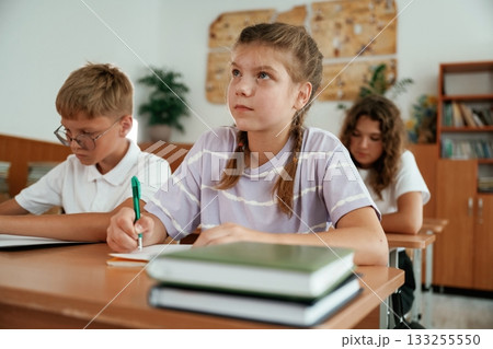 Sitting by the desks. Pupils, kids in the classroom together 133255550