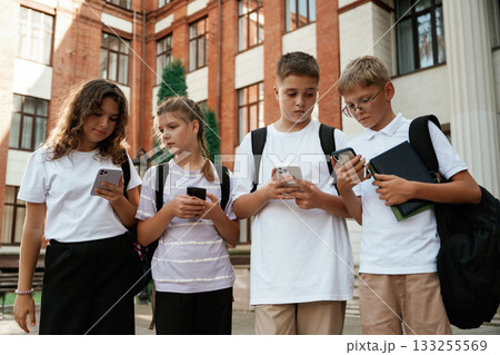 With smartphones, standing. Kids are near the school together, pupils 133255569