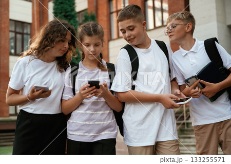 With smartphones, standing. Kids are near the school together, pupils With smartphones, standing. Kids are near the school together, pupils 133255571