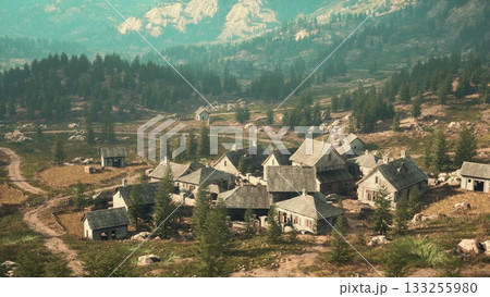 A serene village sits nestled among tall trees and dramatic mountains. Warm golden light bathes the rustic homes, creating a peaceful atmosphere during late afternoon. 133255980