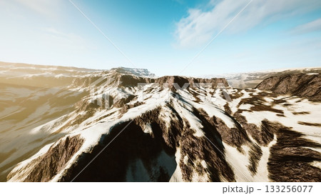 Majestic mountains covered in snow stretch across the horizon, illuminated by sunlight. The clear blue sky contrasts with the rugged terrain, creating a peaceful winter scene. 133256077