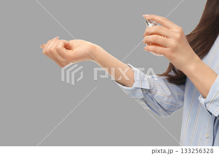 A woman is spraying her wrist with perfume in a bright setting 133256328