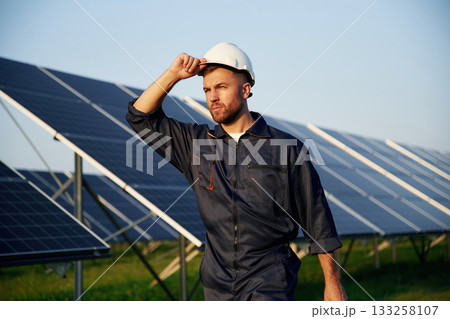 Touching the white hard hat. Man is working with solar panels outdoors at daytime Touching the white hard hat. Man is working with solar panels outdoors at daytime 133258107