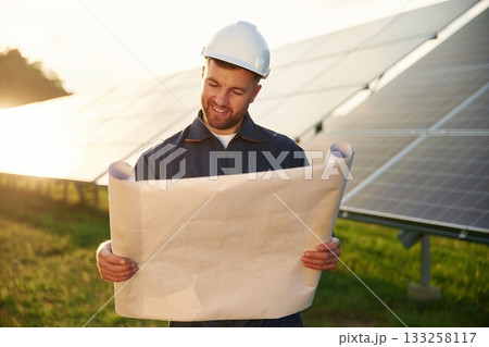 Paper plan in hands. Man is working with solar panels outdoors at daytime Paper plan in hands. Man is working with solar panels outdoors at daytime 133258117