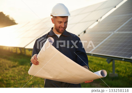 Paper plan in hands. Man is working with solar panels outdoors at daytime Paper plan in hands. Man is working with solar panels outdoors at daytime 133258118