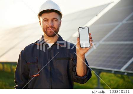 Smartphone with copy space on it. Man is working with solar panels outdoors at daytime Smartphone with copy space on it. Man is working with solar panels outdoors at daytime 133258131