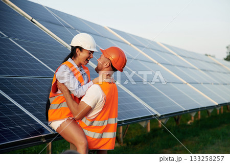 Playful mood, embracing each other. Man and woman, workers are near solar panels, in uniform Playful mood, embracing each other. Man and woman, workers are near solar panels, in uniform 133258257